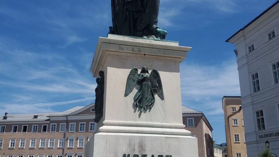 A monumental bronze statue of Mozart standing in a plaza in Salzburg, Austria, under a clear blue sky.