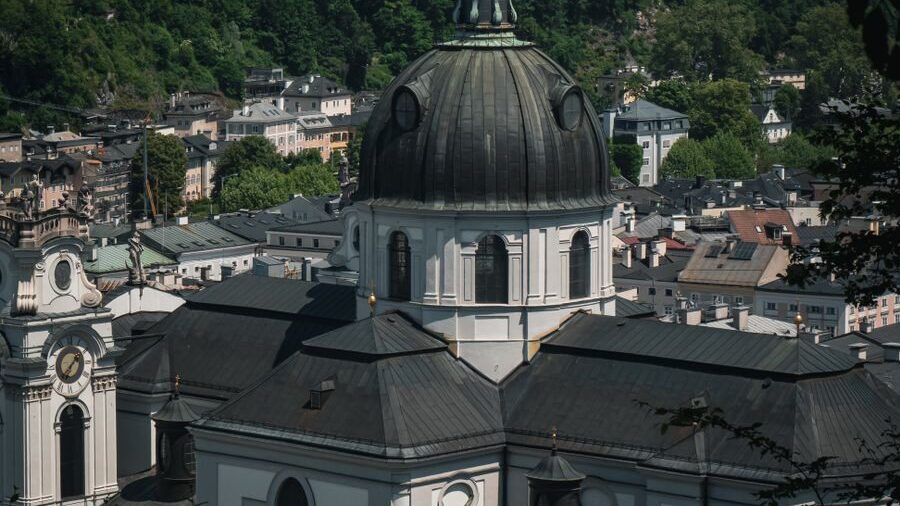 Photo by Jcmotive Aerial view of Salzburg Cathedral's dome surrounded by the Austrian cityscape and lush greenery.