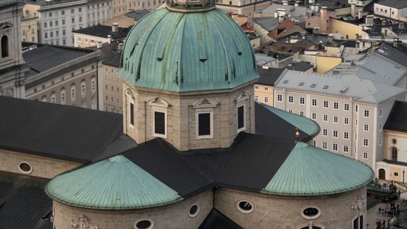 Photo by Nicola Raviglione A stunning drone shot of Salzburg's historic DomQuartier Cathedral against the urban cityscape.