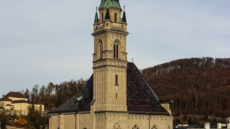 Gothic-style church tower rises above city rooftops with hill backdrop.