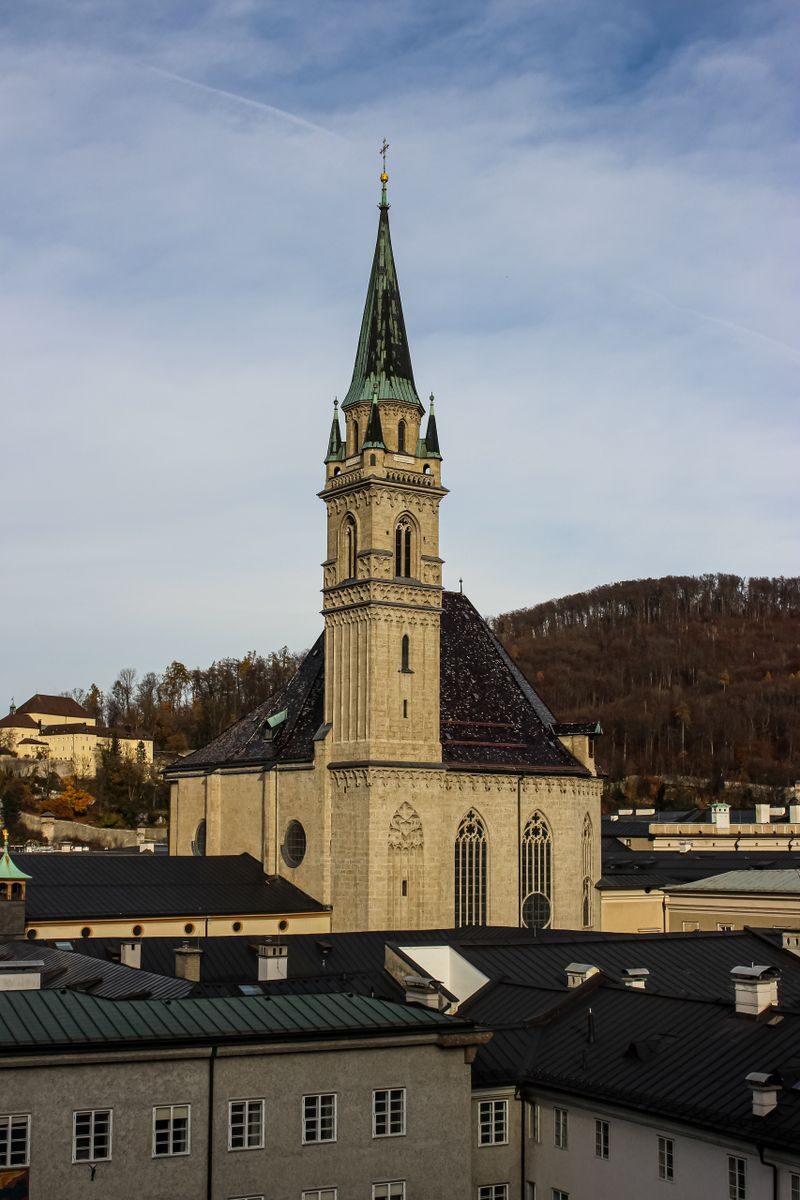 Gothic-style church tower rises above city rooftops with hill backdrop.
