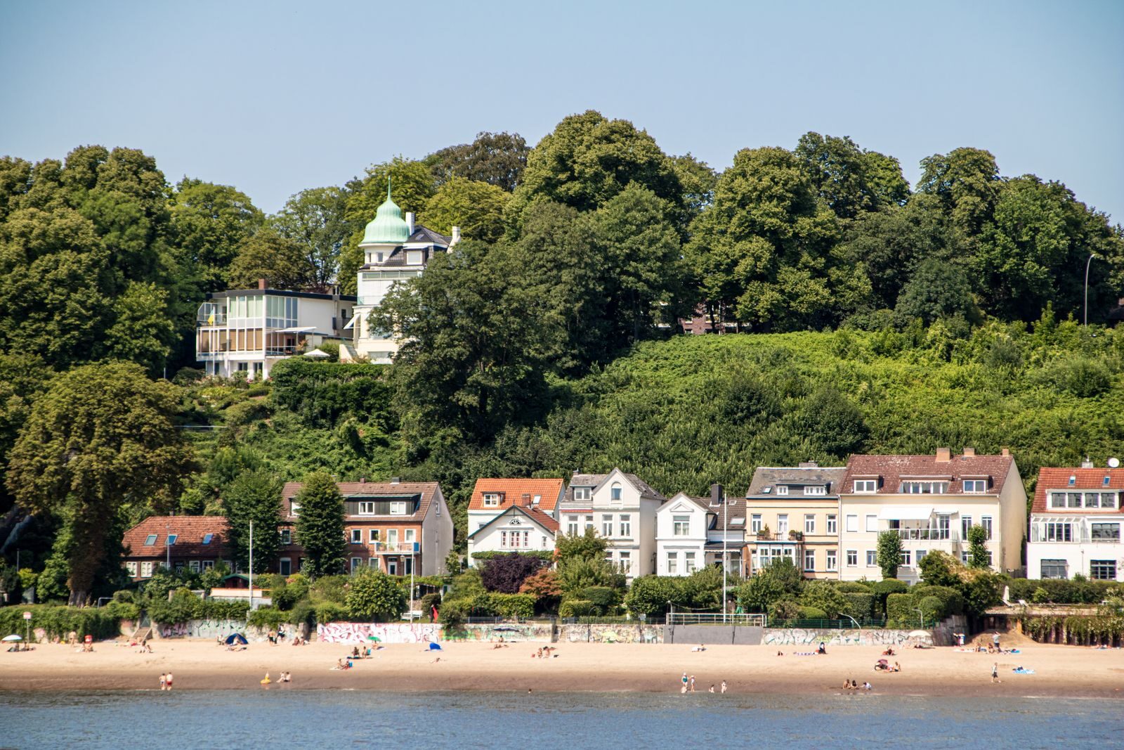 Charming view of Blankenese's waterfront with historic houses and lush greenery under a clear summer sky.